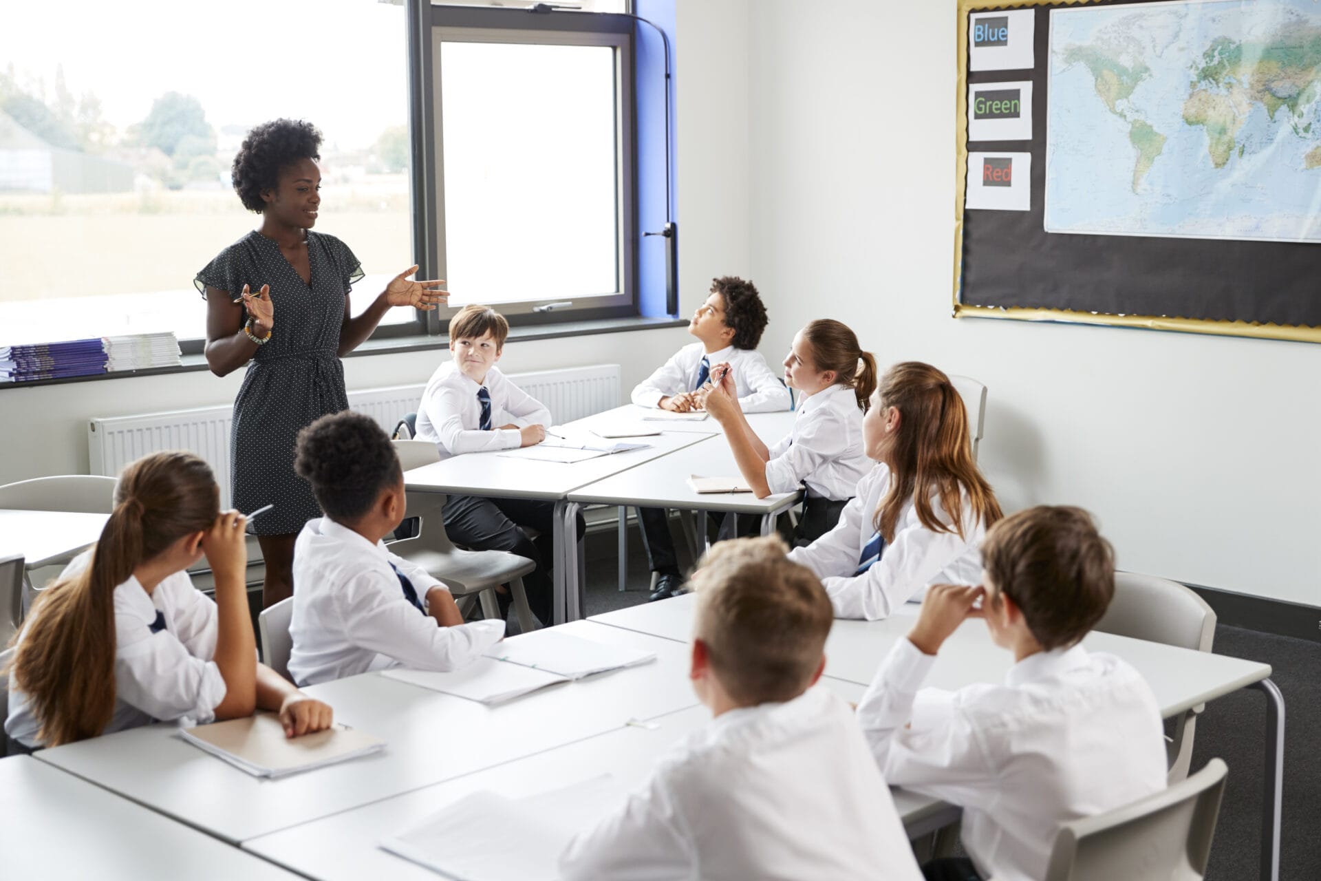 Female High School Tutor Standing By Tables With Students Wearing Uniform Teaching Lesson