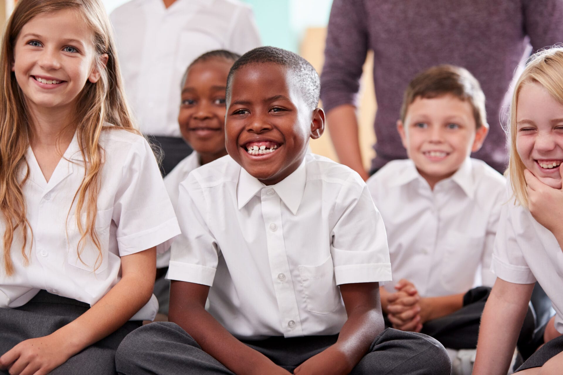 Group Of Elementary School Pupils Wearing Uniform Sitting On Floor Listening To Teacher