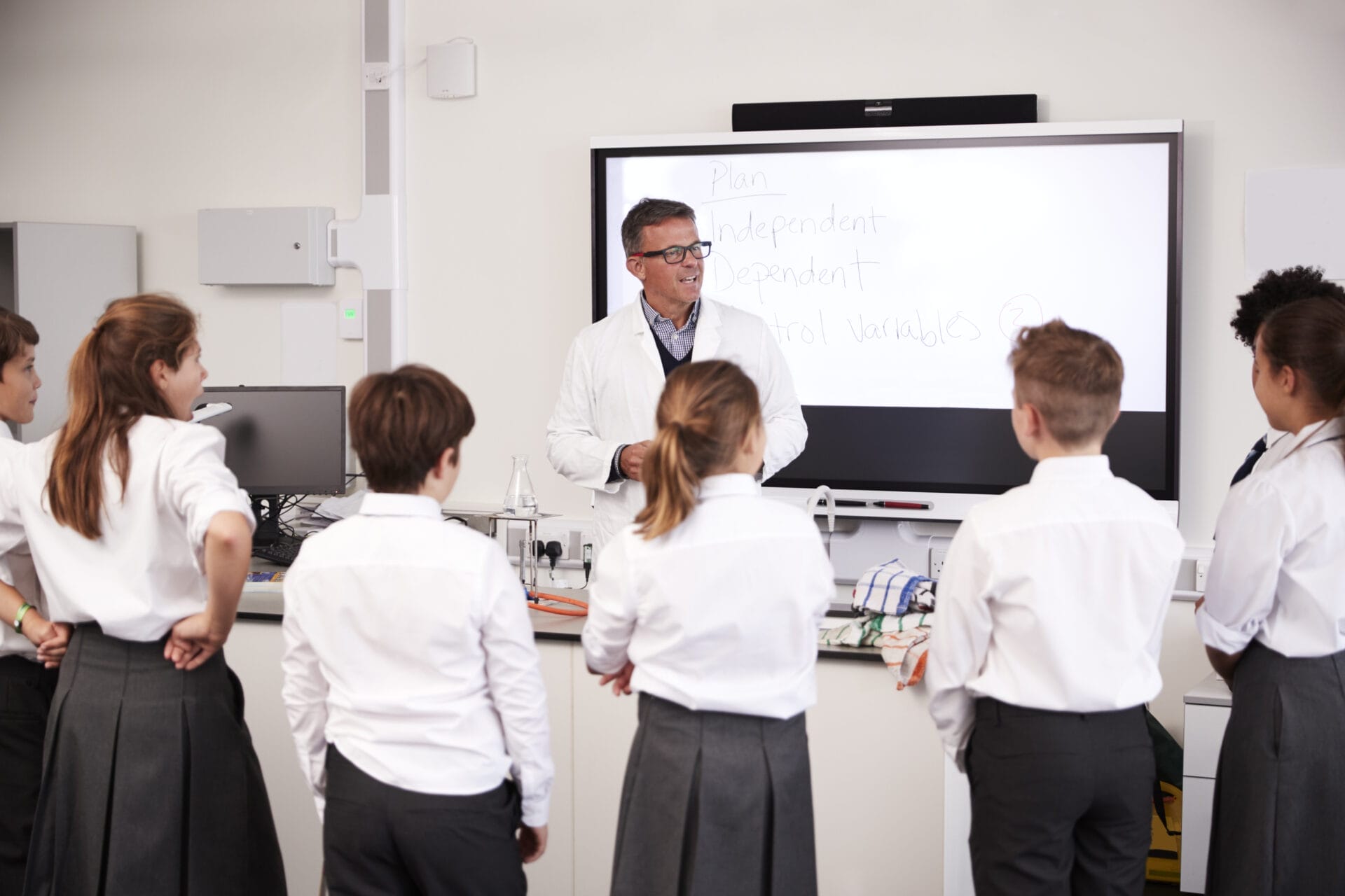 Male High School Tutor Teaching High School Students Wearing Uniforms In Science Class